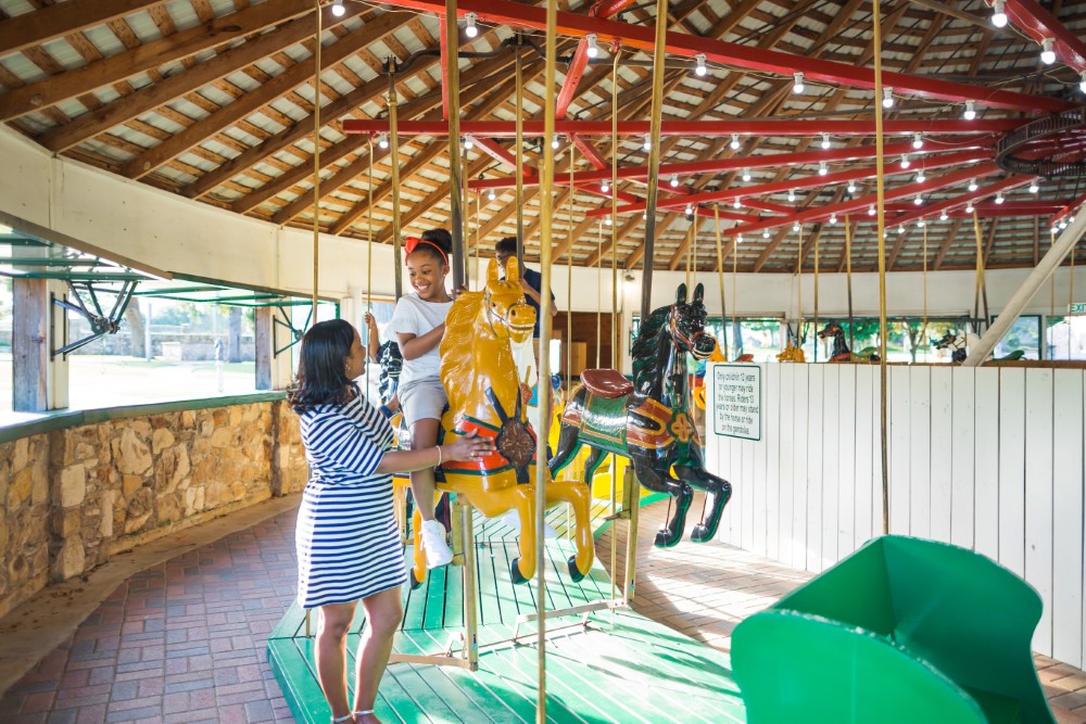 mom with daughter riding on a hobby horse on the carousel at fireman's park